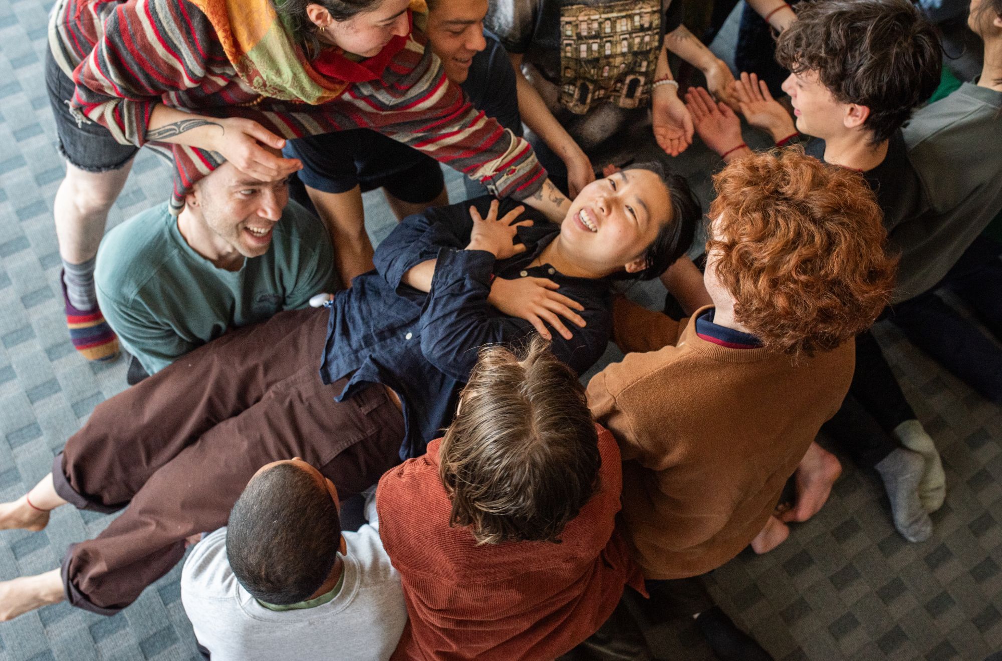 Overhead view of a group gently holding up a laughing person lying across their arms.