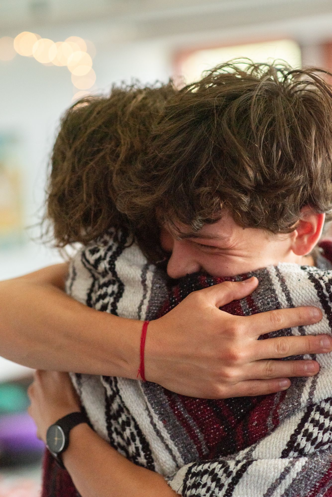 Two people in a tight hug, one wrapped in a striped woven blanket.