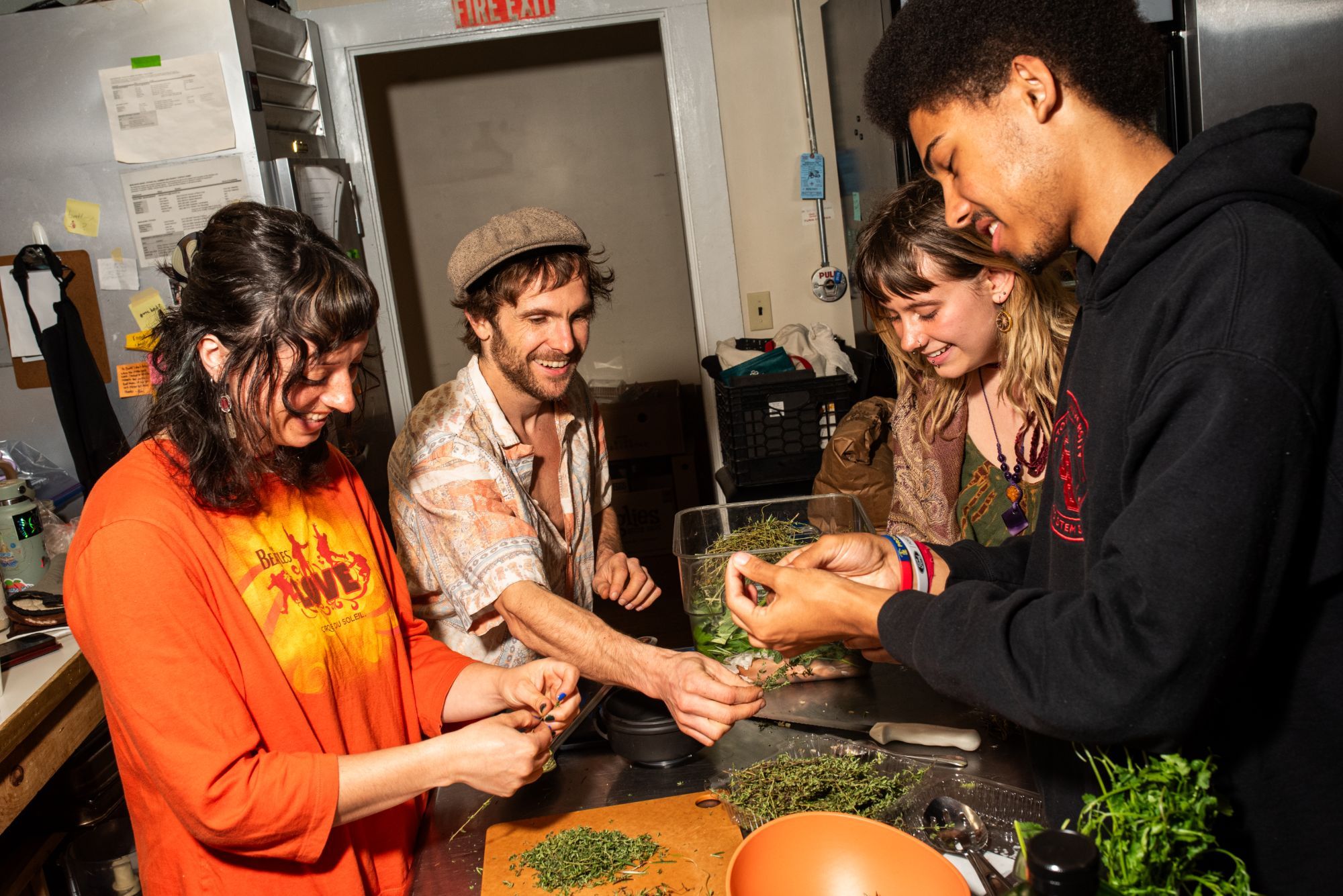 Four people at a kitchen counter, smiling as they strip fresh thyme and herbs together.