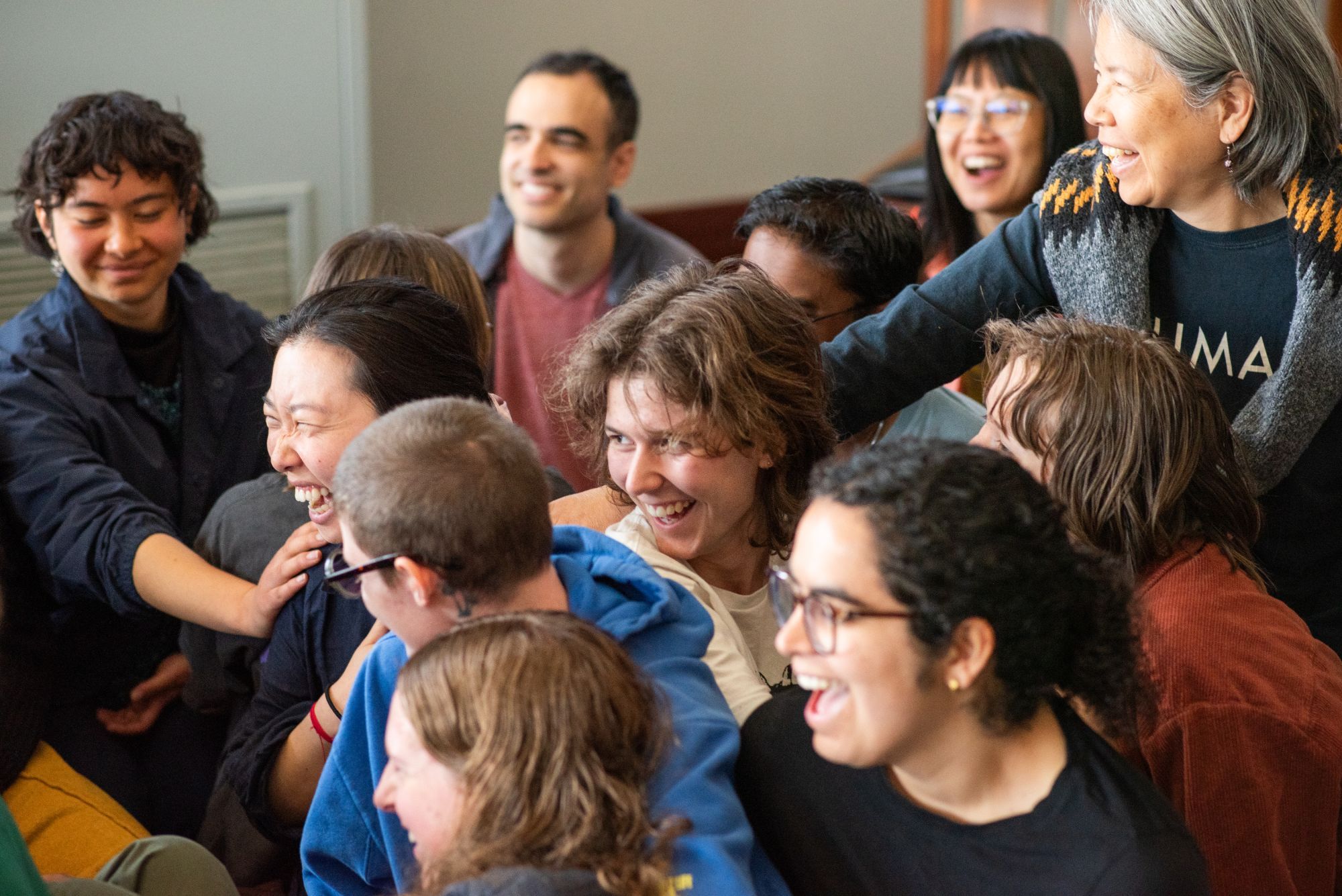 A crowd of young people and elders pressed close together, laughing, with hands on one another's shoulders.